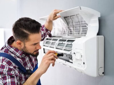 Happy Male Technician Repairing Air Conditioner With Screwdriver